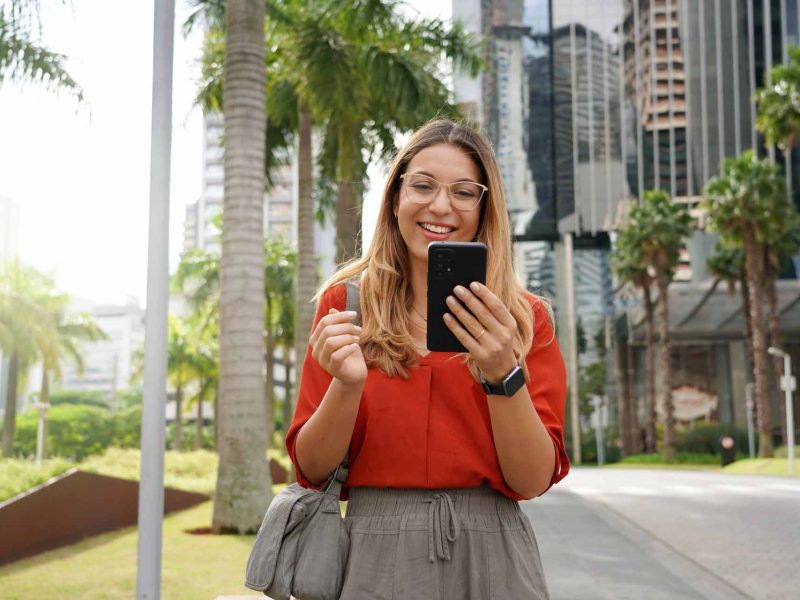 Young businesswoman using phone when walking outside office